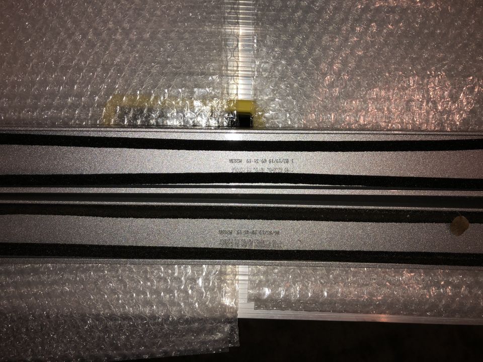 Two silver roof rack rails wrapped in bubble wrap, with black rubber trim and stamped serial numbers