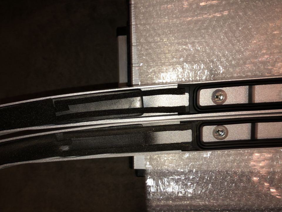 Pair of black and silver roof rack crossbars, one above the other, with foam padding and visible mounting hardware