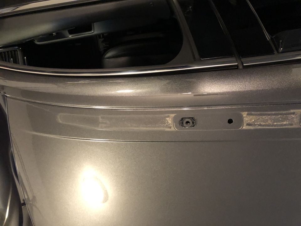 Close-up of a gray vehicle's rear bumper showing a sensor and a small hole