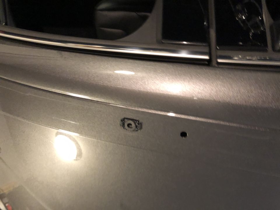 Close-up of a car's metallic gray door panel showing a mounting point for a door handle and a small hole