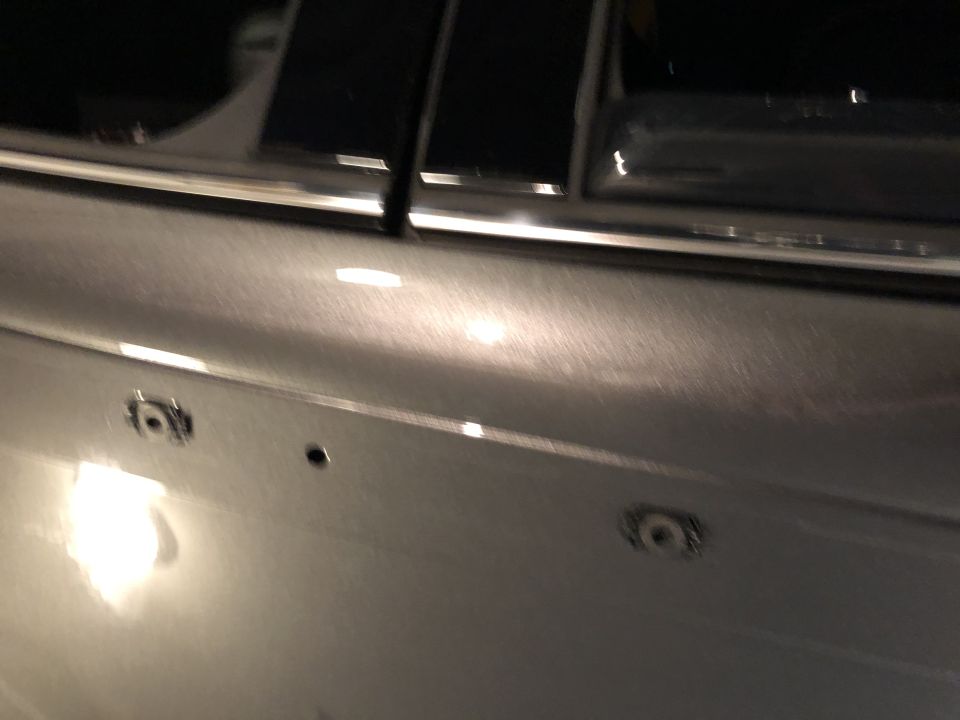 Close-up of a silver car door panel showing three small holes, likely for mounting accessories
