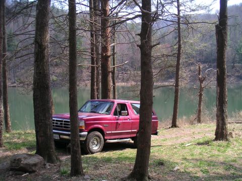1994 Ford Bronco - Red 1994 Ford Bronco parked near a lake surrounded by trees.