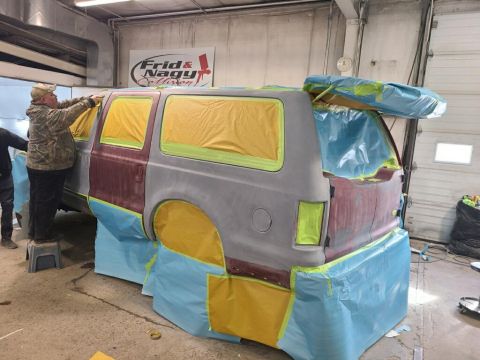 2002 Ford Excursion - SUV being prepped for paint in a workshop, showing masking tape and primer on the body panels.