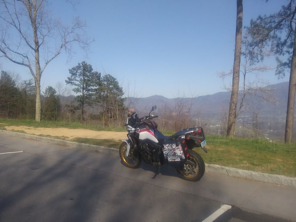 Side view of a white and red motorcycle with saddlebags parked on a roadside with mountains in the background