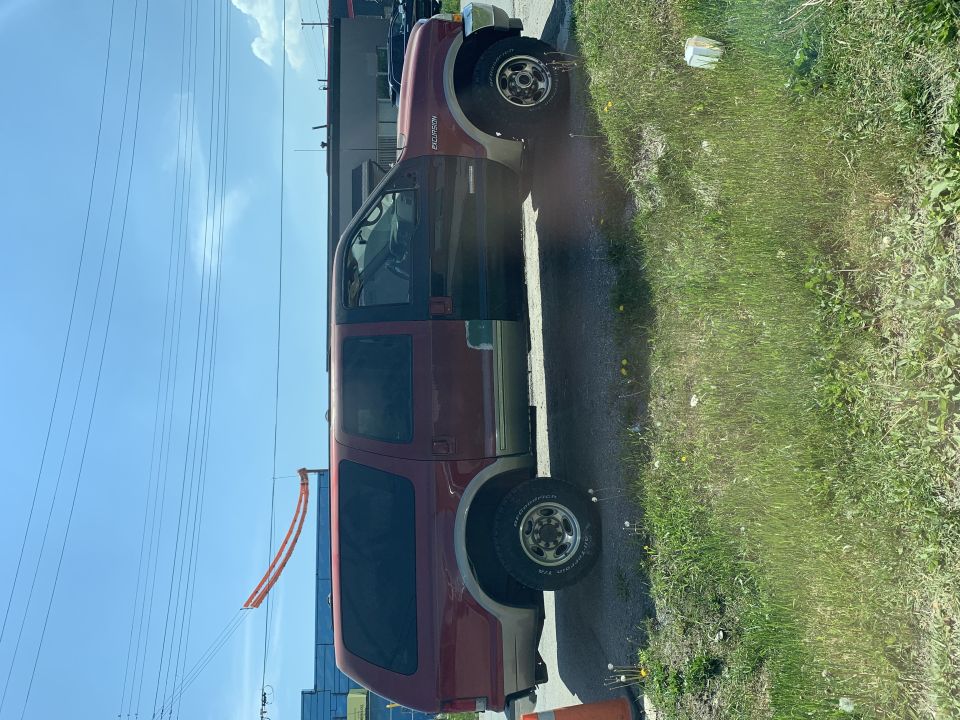 Red and tan Ford Excursion, side view, driver's door open, parked on asphalt next to grass