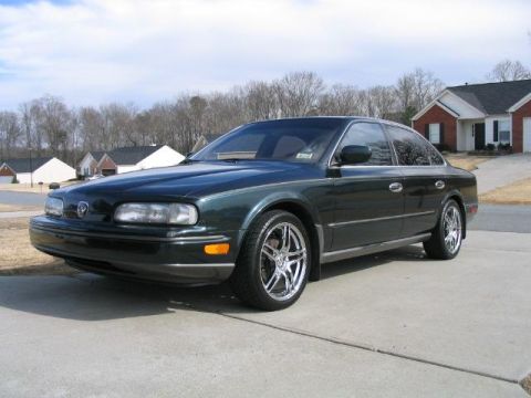 1986 Ford F-150 - A dark green Infiniti Q45 sedan is parked on a concrete driveway in front of houses.