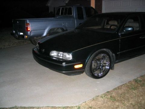1986 Ford F-150 - A dark sedan with custom chrome wheels is parked in a driveway next to a blue pickup truck.