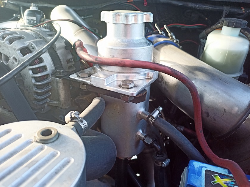 Close-up of engine parts including alternator, hoses, and a silver reservoir
