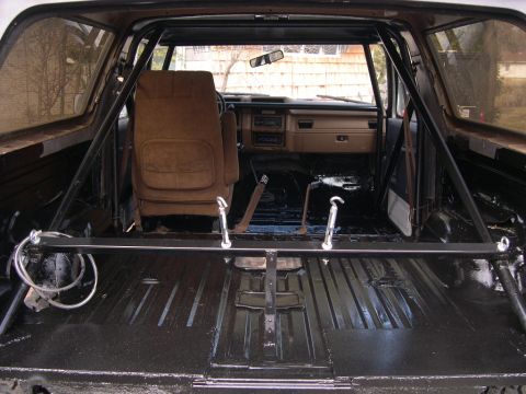 1986 Ford Bronco - The interior of a vehicle shows a roll cage and a bare cargo area, with the front seats and dashboard visible.