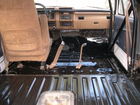 1986 Ford Bronco - The interior of a vehicle shows tan seats and a black painted floor, with a roll cage visible.