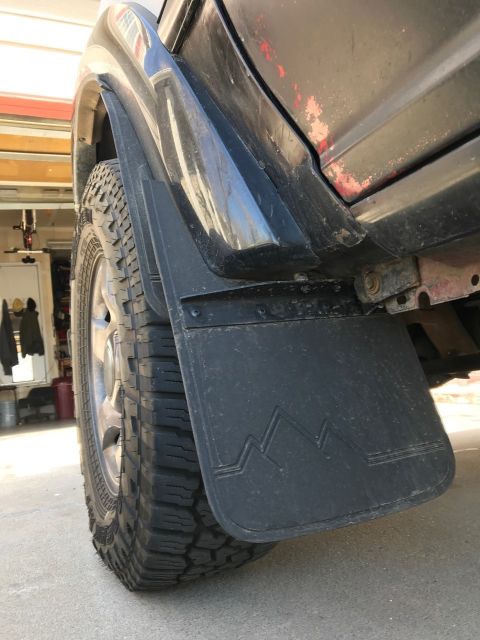 2000 Ford Explorer - A close-up view of a black mud flap with a mountain design, attached to the side of a vehicle near the rear tire.