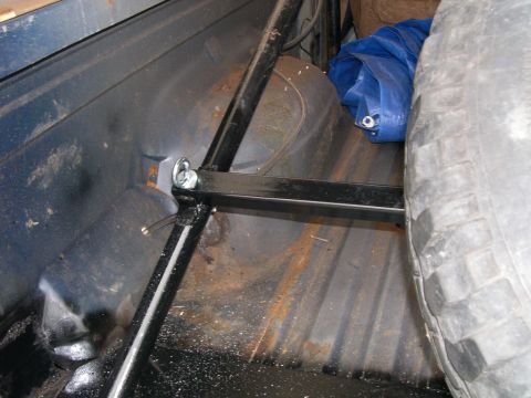 1986 Ford Bronco - The interior of a vehicle's cargo area shows a spare tire, a blue tarp, and metal bracing. The floor appears to be rusty.