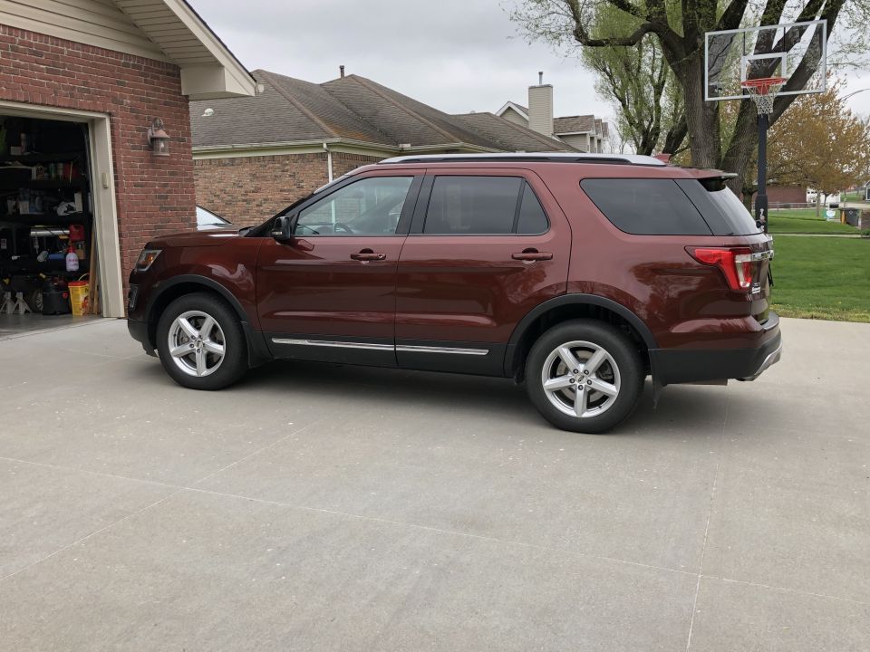 Side view of a maroon Ford Explorer parked in a driveway next to an open garage