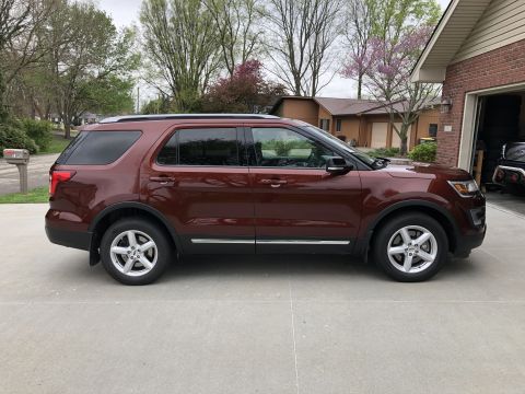 2016 Ford Explorer - The side profile of a red Ford Explorer is captured in this image, parked in front of a residential garage.