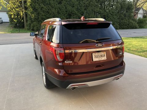 2016 Ford Explorer - 2016 Ford Explorer XLT in red, seen from the rear on a paved surface with trees in the background.