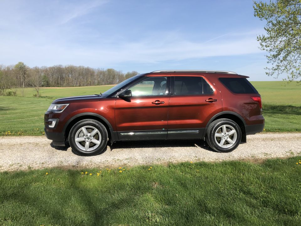 Side view of a 2016 Ford Explorer parked on a gravel road with grass and trees in the background