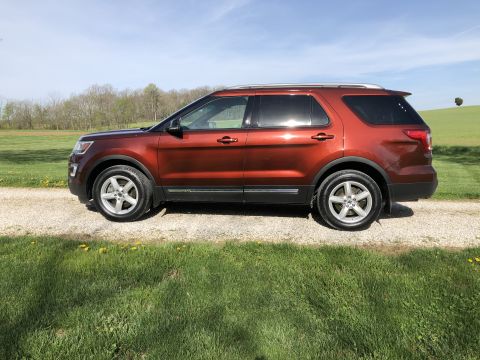 2016 Ford Explorer - This 2016 Ford Explorer is seen from the side, parked on a gravel road with a grassy field and trees behind it.