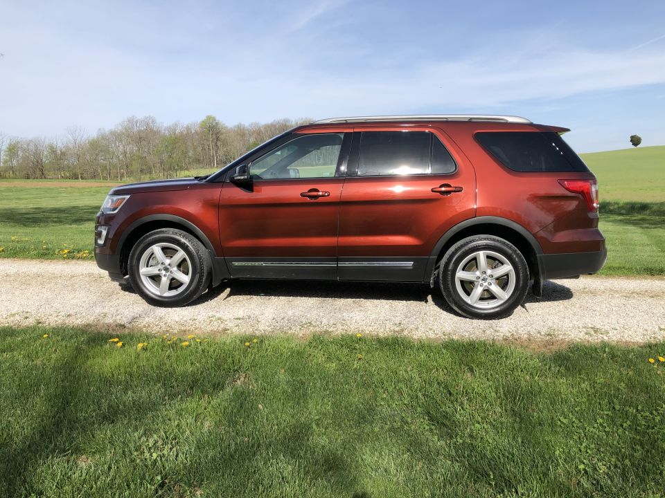 Orange 2016 Ford Explorer SUV parked on a gravel road with grass and trees in the background