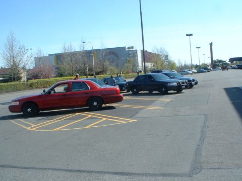 1999 Ford Crown Victoria - A red sedan is parked next to multiple police vehicles under a bright blue sky.