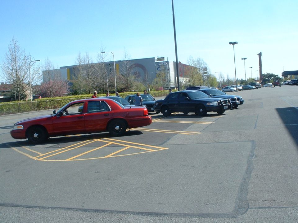 Red Ford Crown Victoria on steel wheels parked beside a black push-bar Crown Vic in a lot