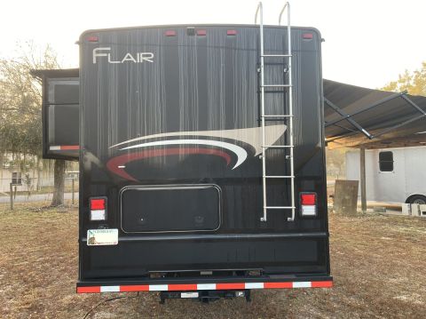 2015 Ford F-550 - Rear view of a black RV with a ladder and slide-out extended.