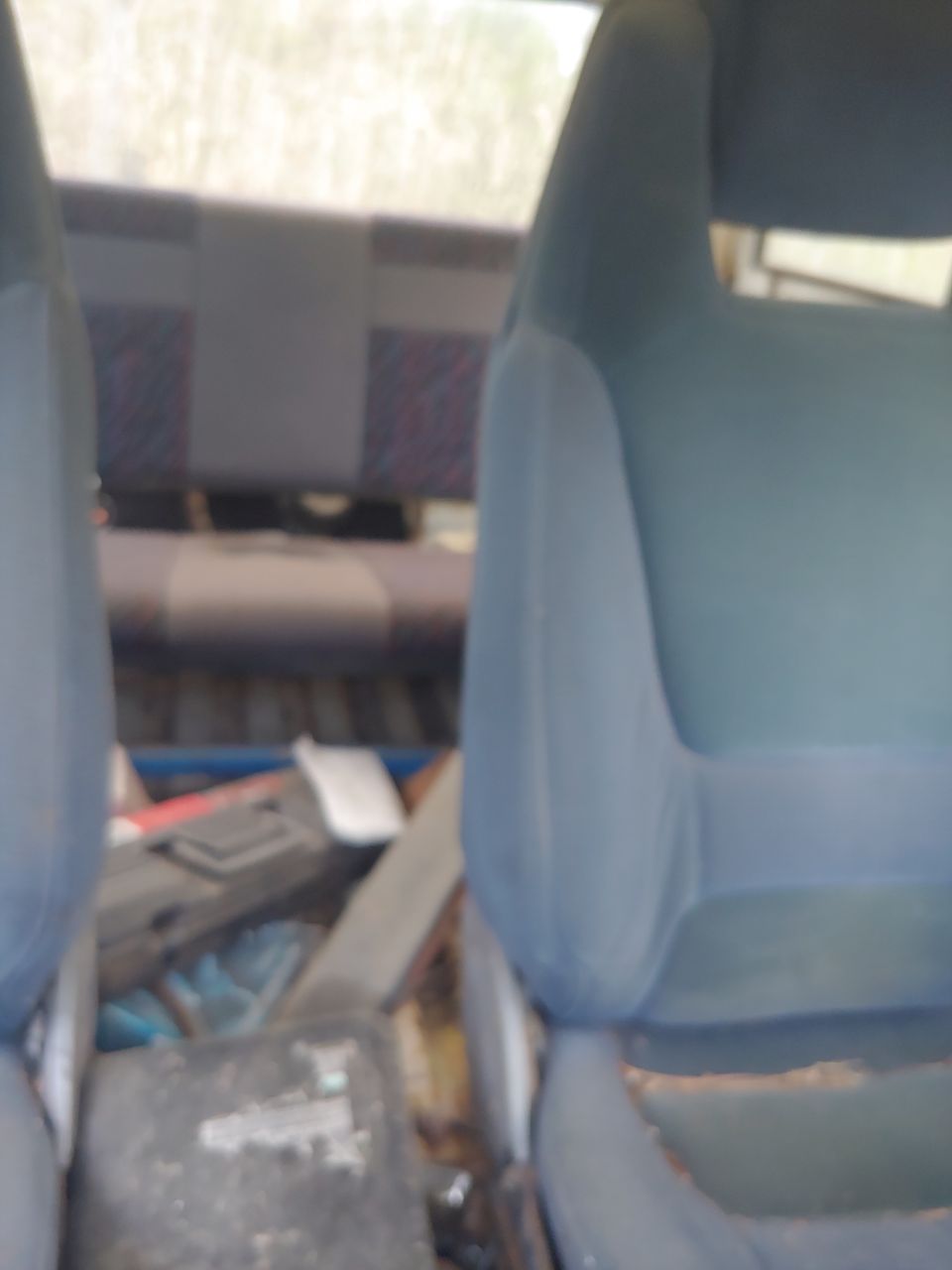 Interior view of a vehicle showing front seats, rear bench seat, and clutter in the back