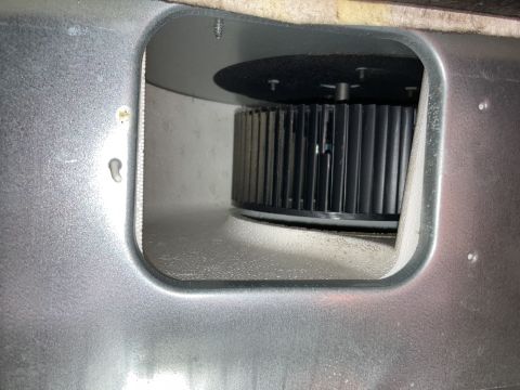 2015 Ford F-550 - Black squirrel-cage blower motor fan seen through a rectangular access opening cut in a silver sheet-metal panel.