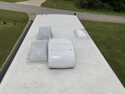 2015 Ford F-550 - Top of a white RV roof showing several plastic vent covers and a rooftop AC unit, grass and driveway in background.