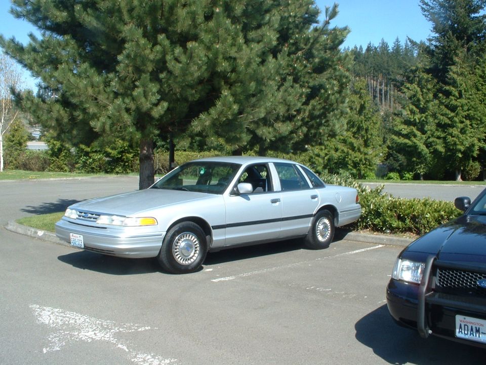 Silver 1999 Ford Crown Victoria parked next to a police car