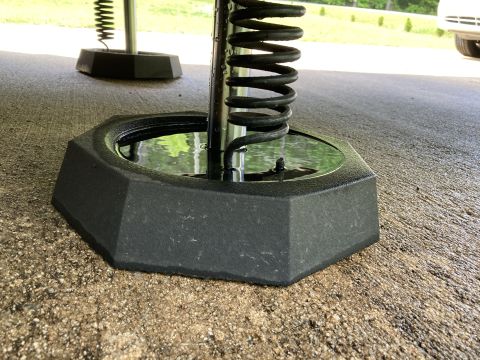 2015 Ford F-550 - Close-up of a black RV leveling jack base on concrete, showing a coiled spring and collected water.