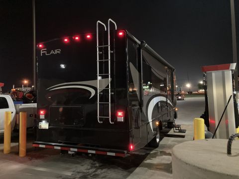 2015 Ford F-550 - Motorhome with 'Flair' badging parked at a gas station with a white truck nearby.