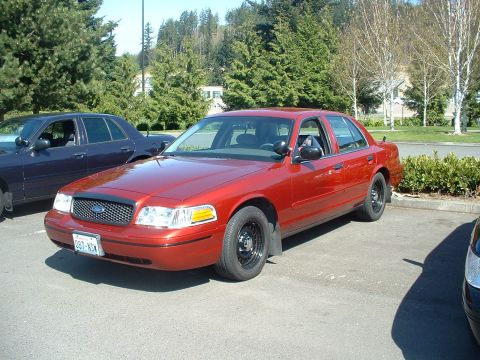 1999 Ford Crown Victoria - A red Ford Crown Victoria is parked in a lot next to another similar vehicle.