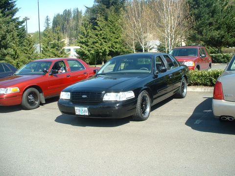 1999 Ford Crown Victoria - A black Ford Crown Victoria is parked in a lot, with other vehicles visible in the background.