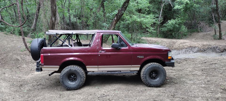 Maroon Ford Bronco with a soft top and spare tire on the back, parked on a dirt trail