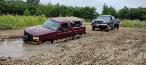 1996 Ford Bronco - A maroon 1996 Ford Bronco is stuck in a mud pit while a green Ford F-Series truck attempts to tow it out.