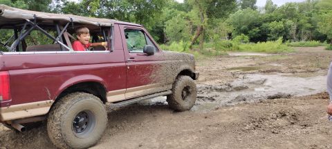 1996 Ford Bronco - Child steers a muddy 1996 Ford Bronco through an offroad park.