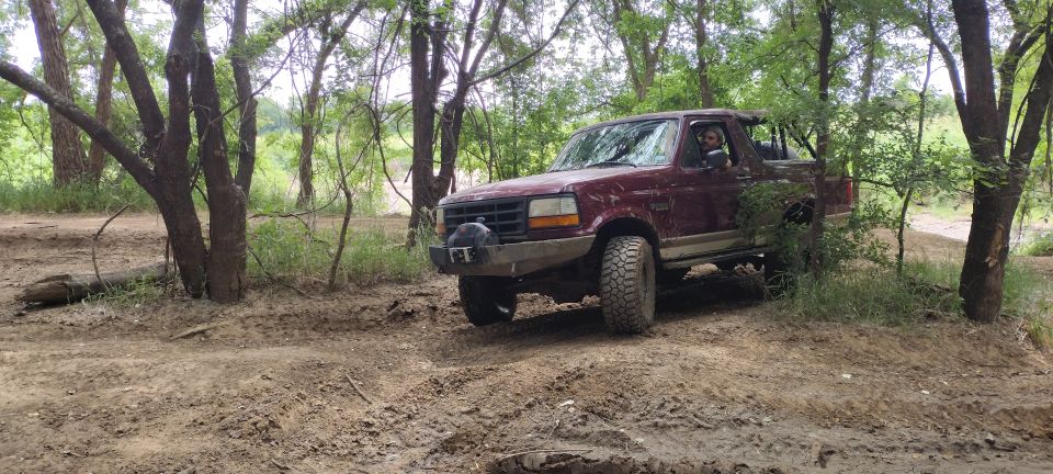 Maroon 1996 Ford Bronco with aftermarket bumper on a muddy trail