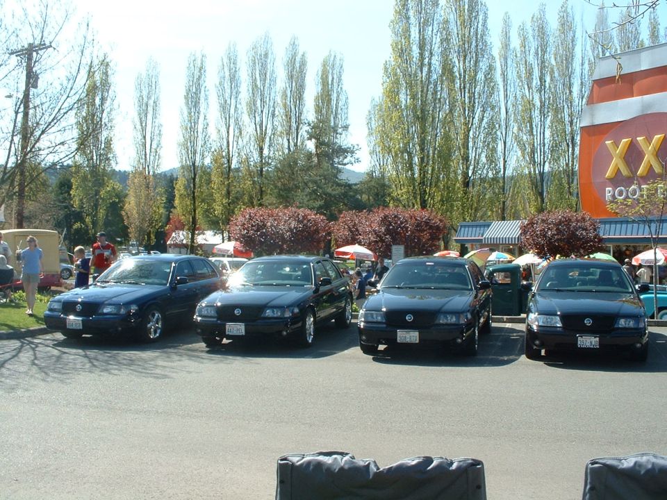 Four dark Ford Crown Victoria sedans parked in a lot, one with a trailer