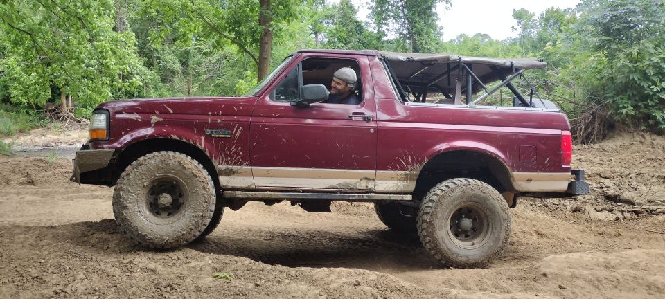 Red 1996 Ford Bronco side view, off-road tires, soft top