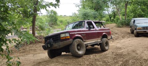 1996 Ford Bronco - Two SUVs navigating a muddy off-road park trail with trees and foliage surrounding them.