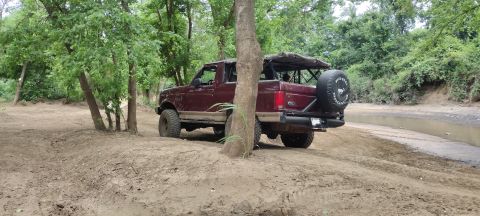 1996 Ford Bronco - This 1996 Ford Bronco is navigating a muddy trail surrounded by lush green trees.