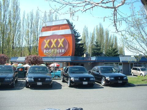 1999 Ford Crown Victoria - Several cars are parked in front of a XXX Root Beer establishment on a sunny day.