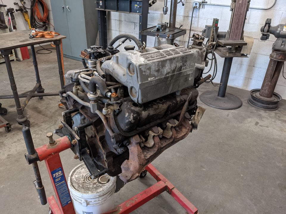 V8 engine on red 750 lb engine stand in a workshop, white bucket underneath