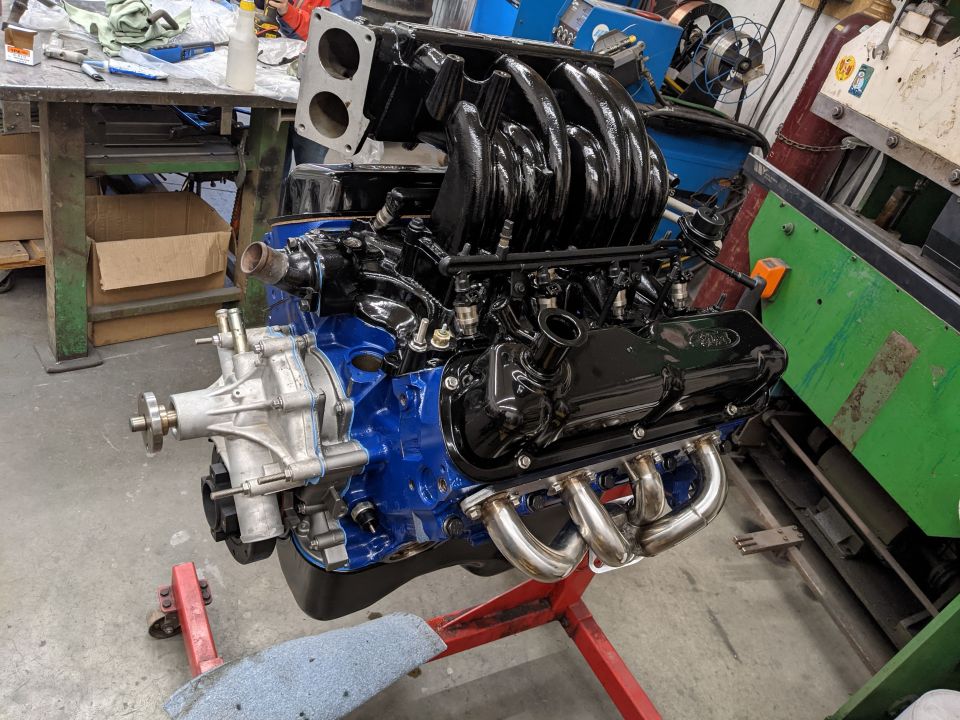 Blue engine block with black intake manifold and exhaust headers on a red engine stand