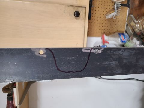 1985 Ford Bronco - A metal bracket with a drawn outline and two holes, one of which has a bolt. The background shows a workbench area.