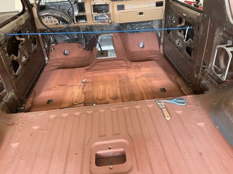 1984 Ford Bronco - The interior of a 1980s SUV is shown with the floor prepped for restoration, revealing its stripped-down state.