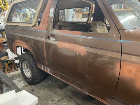 1984 Ford Bronco - This 1984 Ford Bronco is in a garage, showing signs of repair work with primer visible on its brown body.