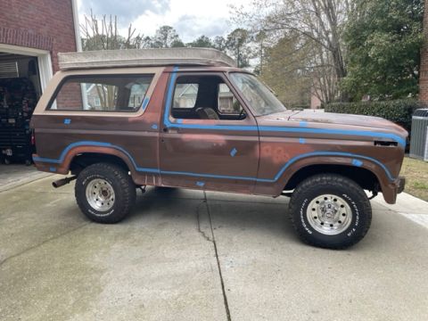 1984 Ford Bronco - Side view of a brown Ford Bronco, possibly undergoing restoration, with a mattress secured to its roof.