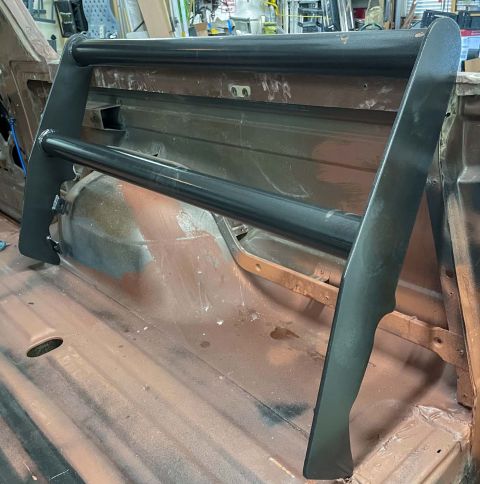 1984 Ford Bronco - A black roll bar is mounted inside the bed of a pickup truck, likely a Ford Bronco, awaiting further restoration.