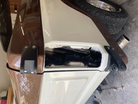 1984 Ford Bronco - A close-up view of a vehicle's exterior, focusing on a body panel with an open section and a tire visible.